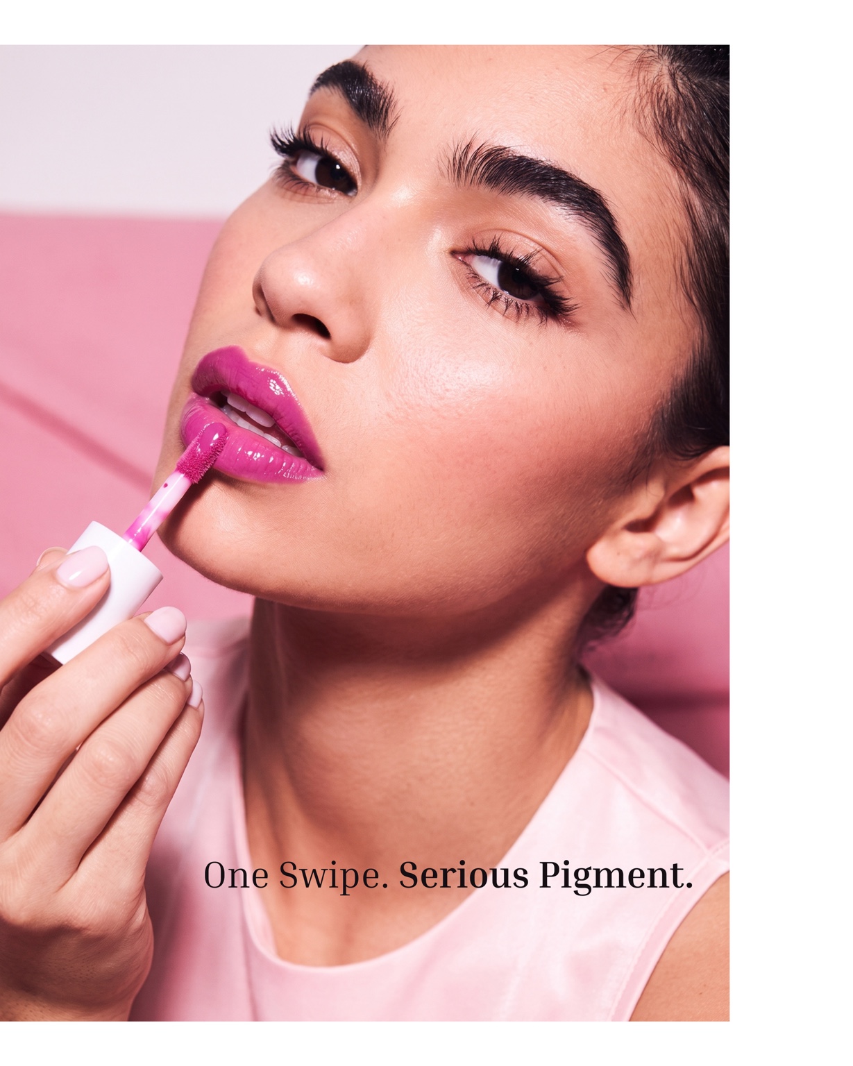 A model applying a bright fuchsia lip gloss, with the line “One Swipe. Serious Pigment.”